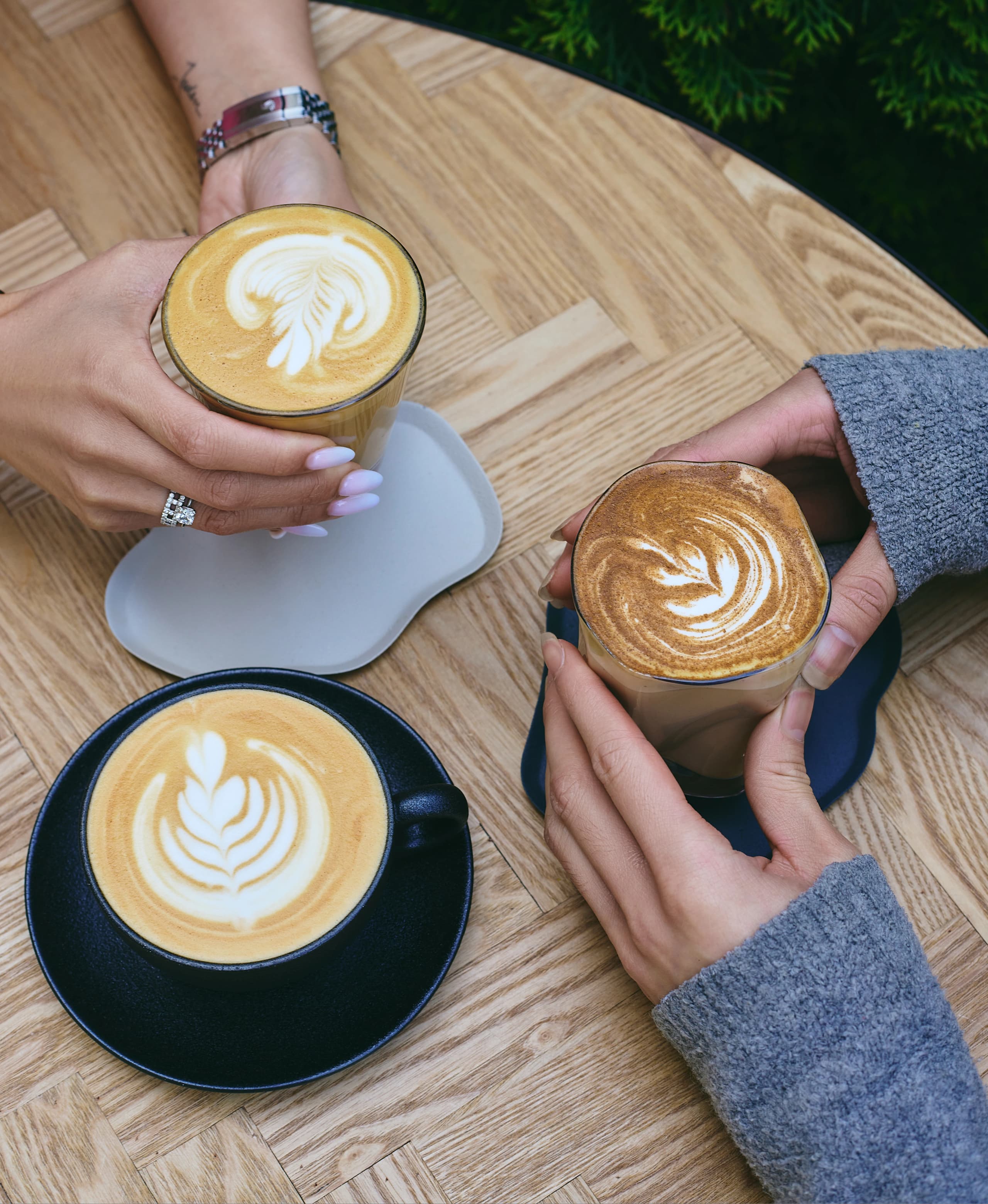 Three lattes held at a wooden table - 1407 Breakfast Club